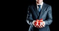 Gift man. Happy young businessman holding surprise gift box present with red ribbon isolated on black background. Black Royalty Free Stock Photo