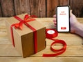 Gift parcel or mail box with ribbon red bow and mobile phone in hand, brown carton parcel, surprise, online shopping concept