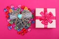 Gift in a pink box on crimson background and wicker decorative heart beside. Gift box with wicker heart beside surrounded with Royalty Free Stock Photo