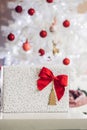 Gift with red bow in front of white christmas tree, decorated wi Royalty Free Stock Photo