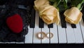 Gift to the beloved woman, yellow roses lie on the piano with engagement ring and a red box in the shape of a heart on black lace, Royalty Free Stock Photo