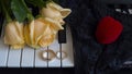 As a gift to the beloved woman, yellow roses lie on the piano with engagement ring and a red box in the shape of a heart on black Royalty Free Stock Photo