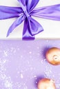 Gift with violet ribbon and bow-knot, Christmas balls, snow on a violet background. Copy space