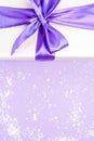 Gift with violet ribbon and bow-knot, snow on a violet background. Copy space