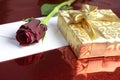 Gift wrapped in gold paper, red rose and a blank envelope