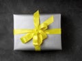 Gift wrapped in gray paper on a dark gray background. Yellow ribbon. Colors of the Year 2021: Solid gray, brightening