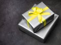 Gift wrapped in gray paper on a dark gray background. Yellow ribbon. Colors of the Year 2021: Solid gray, brightening