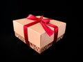 Gift in a box with a red ribbon on a black background. Beige gift box with a red satin ribbon and bow Royalty Free Stock Photo