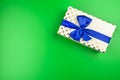 A gift wrapped in white paper with gold circles wrapped in a blue ribbon tied in a bow, isolated on a green background, top view. Royalty Free Stock Photo