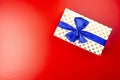 A gift wrapped in white paper with gold circles wrapped in a blue ribbon tied in a bow, isolated on a red background, top view. Royalty Free Stock Photo