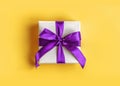 Gift wrapped in white paper with a violet bow made of satin on soft yellow background Royalty Free Stock Photo