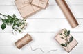 Gift wrapping background, copy space. Rolls of kraft wrapping paper, twine, branch of roses, gift boxes on wooden background