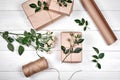 Gift wrapping background. Rolls of kraft wrapping paper, twine, branch of roses, gift boxes on wooden background, copy space.