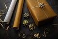 Gift wrapping. wrapped golden present with wrapping paper rolls and accessories on dark background