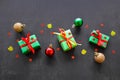 Gifts in green paper with red and yellow ribbons, gold, red and green christmas balls and confetti in the form of red stars lie in Royalty Free Stock Photo