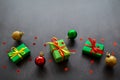 Gifts in green paper with red and yellow ribbons, gold, red and green christmas balls lie in a row. Confetti in the form of red Royalty Free Stock Photo