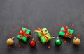 Gifts in green paper with red and yellow ribbons, gold, red and green christmas balls lie in a row. Confetti in the form of red Royalty Free Stock Photo