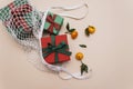 Gifts with ribbons are in a white eco-friendly string bag on a beige background, next to orange ripe tangerines with leaves