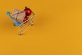 Gifts in a small shopping trolley on a yellow background, concept, copy space Royalty Free Stock Photo