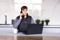 Gig economy concept. Young man freelancer working remotely at home, looking at laptop and consulting client via cellphone, sitting Royalty Free Stock Photo