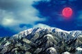 Gigantic super red moon winter landscape highlighting the snow caped mountains of winter.