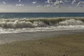 Gigantic Turquoise and deep green swells crashing into a pebbled beach on a blue sky summer day in Sicily