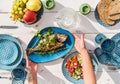 Gilt-head bream also known as Orata grilled on a barbeque grill served by a woman on a white wooden table with vegetable salad and