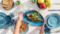 Gilt-head bream also known as Orata grilled on a barbeque grill served by a woman on a white wooden table with vegetable salad and