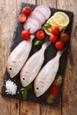 Gilt-head sea bram fish with ingredients close-up on a slate board. Vertical top view