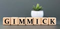 GIMMICK - word on wooden cubes on a gray background with a cactus Royalty Free Stock Photo