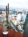 Gin tonic cocktail drink on wooden table with a lime, ice and two straws in rooftop bar with city view Royalty Free Stock Photo