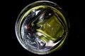 Gin tonic: View from above on isolated round cocktail glass rim with yellow green shimmering ice cubes with lemon and cucumber.