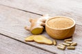 Fresh ginger slice and powder capsules with ginger ground in wooden bowl isolated on wood table .