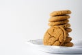 A ginger cookie leans against a stack of ginger cookies on a white plate and a white background with copy space Royalty Free Stock Photo