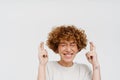 Ginger curly woman posing with fingers crossed for best luck