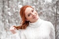 Ginger european girl in white sweater in winter forest. Snow december in park. Christmas magic time.