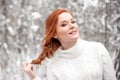 Ginger european girl in white sweater in winter forest. Snow december in park. Christmas time.