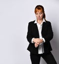 Ginger female in white shirt and black pantsuit. Looking at her hand watch while posing isolated on white background. Close up