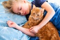 Ginger fluffy cat with little sleeping girl on the blue bed