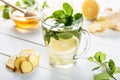 Ginger green tea in a glass for flu cold winter days. Side view on white wooden background decorated with mint, lemon