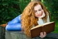 Ginger-haired woman reading a book in park lying on the bench Royalty Free Stock Photo