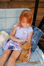 Ginger kitten lies near the girl on the garden swing. The girl strokes her pet. Little blonde caucasian girl with a red cat Royalty Free Stock Photo