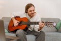 Ginger man playing guitar and using laptop while sitting on couch Royalty Free Stock Photo
