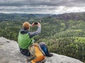 Ginger man takes photos with smart phone on rocky peak