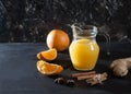 Ginger-orange juice in a glass pitchers, oranges, ginger and cinnamon on a black background. Fresh drink. Healthy eating