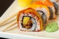 Ginger sushi rolls with decorations and sushi sticks served on a white tray