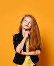 Ginger teenage child in black jacket and pants, yellow t-shirt. She is looking thoughtful, posing on orange background. Close up