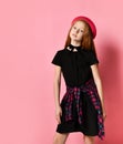 Ginger teenage girl in black dress, checkered shirt on waist, red hat and choker. She smiling, posing on pink background. Close up