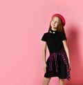 Ginger teenage girl in black dress, checkered shirt on waist, red hat and choker. She smiling, posing on pink background. Close up