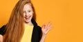 Ginger teenage girl in black jacket, pants, yellow t-shirt. She smiling, showing okay sign, posing on orange background. Close up